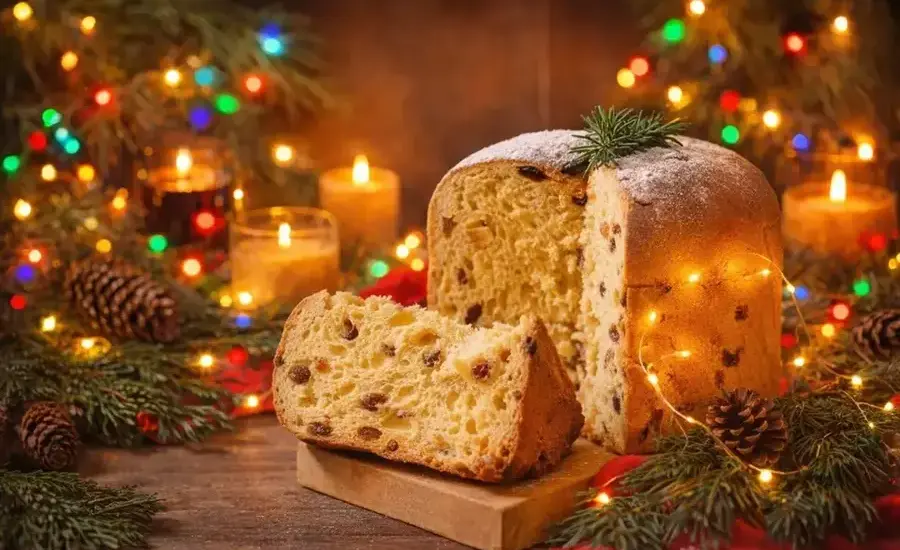 Panettone affettato in atmosfera natalizia tra luci colorate e aghi di pino